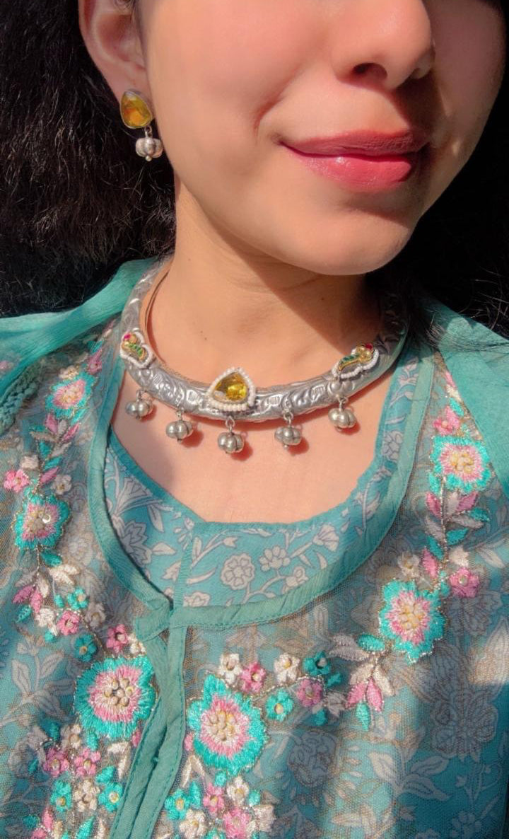 Woman wearing a teal embroidered outfit with jewelry, including earrings and a necklace.